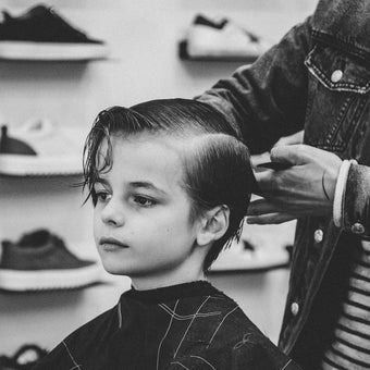 Boy getting a haircut at a barber shop; black and white photo.