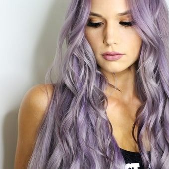 Woman with long wavy lavender hair, wearing a black top, looking down.