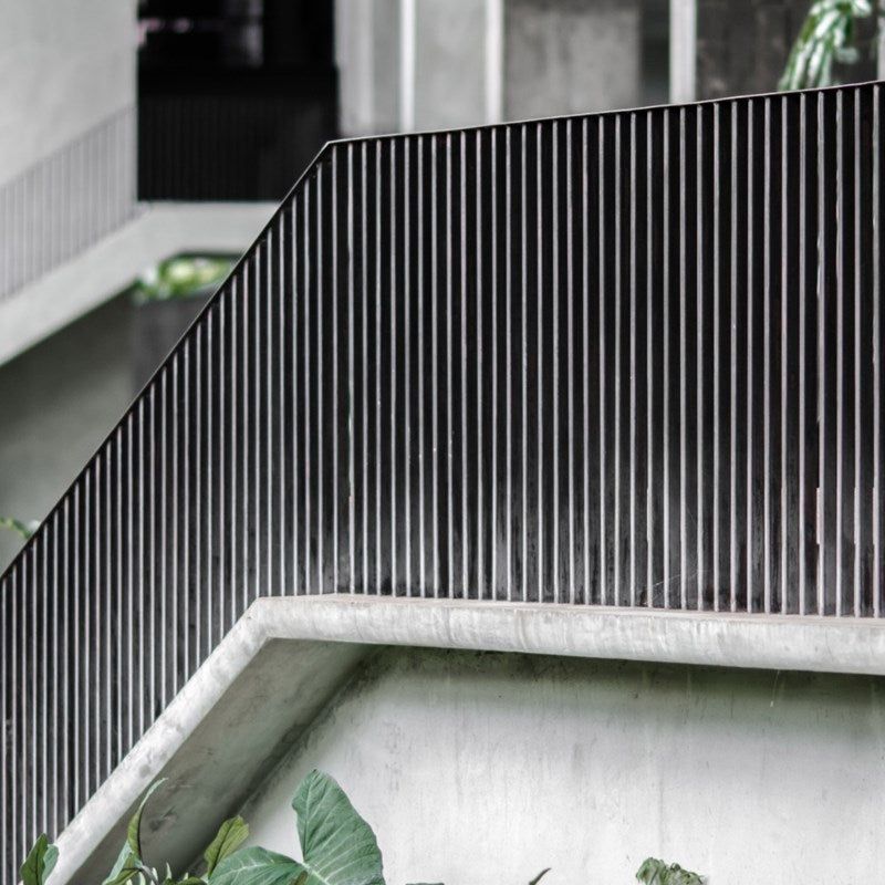 Black vertical bars of a railing on a concrete wall. Green plants are in the foreground.