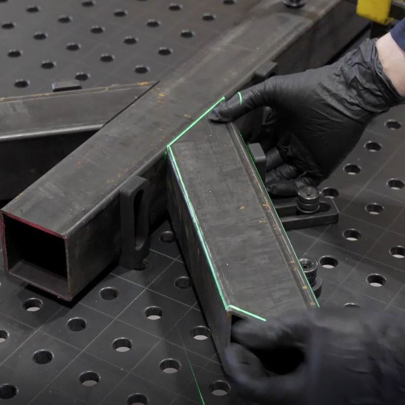 Hands in black gloves aligning metal beams using a laser level, set on a metal table.