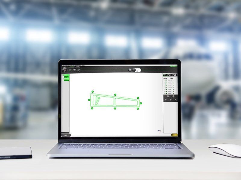 Laptop displaying a 2D CAD drawing, white mouse on desk, factory background.