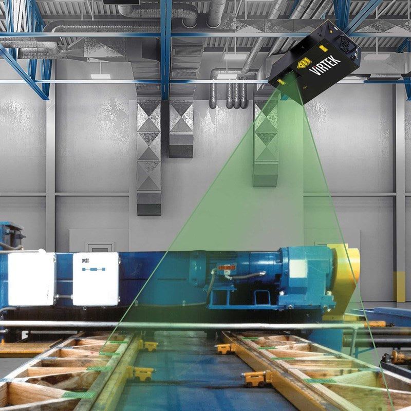 A machine vision sensor scans industrial equipment on a factory floor with a green laser beam.