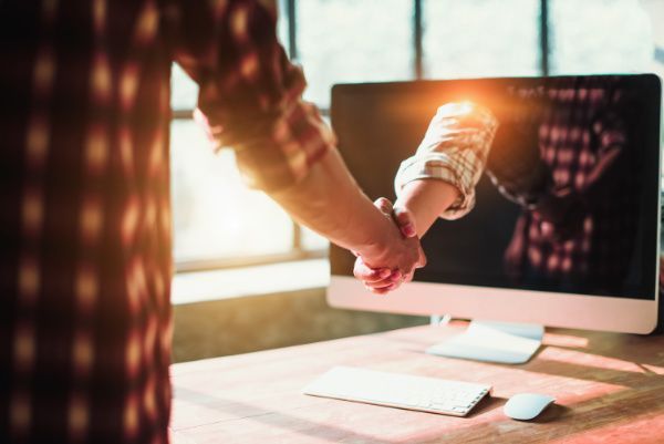 a hand coming through a computer shaking the hand of a blue collar worker wearing a red and black flannel