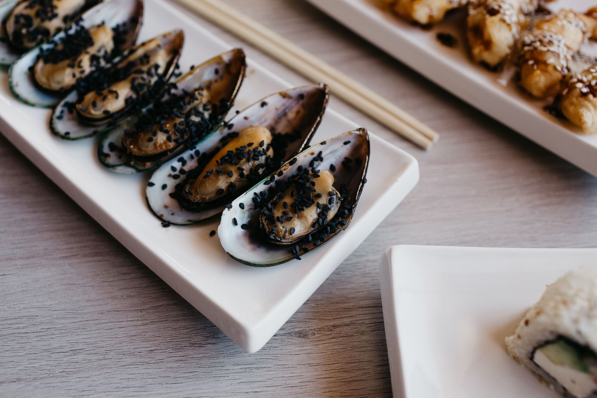 Un piatto bianco condito con cozze e bacchette su un tavolo.
