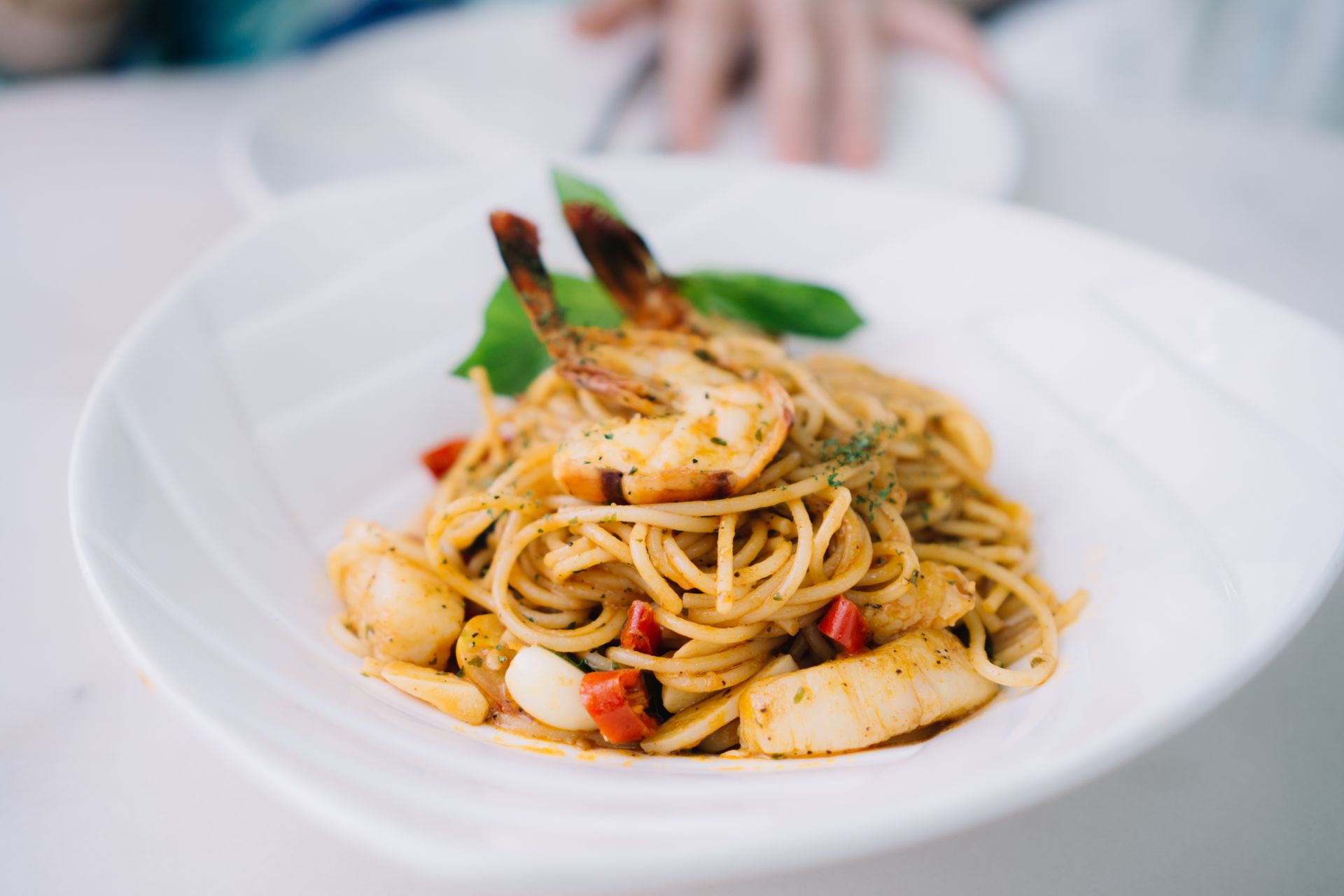 Un piatto bianco condito con spaghetti e gamberetti su un tavolo.