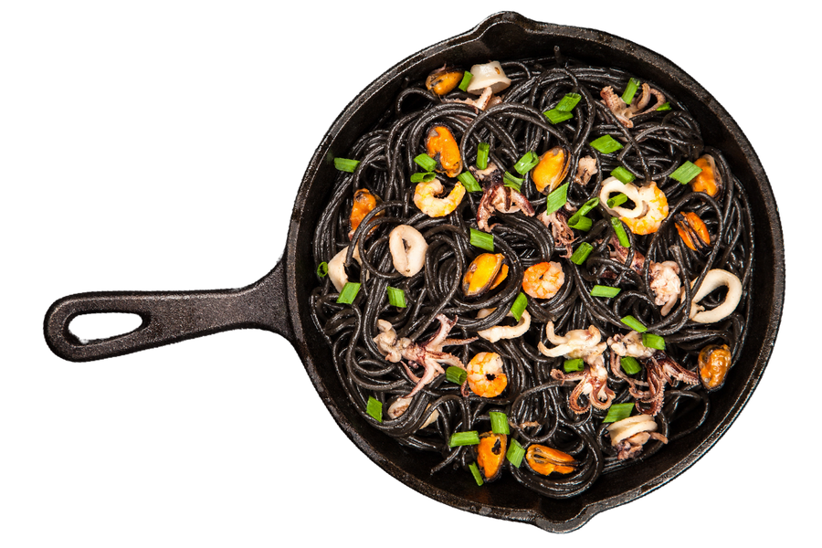 Una padella piena di tagliatelle e frutti di mare su sfondo bianco.