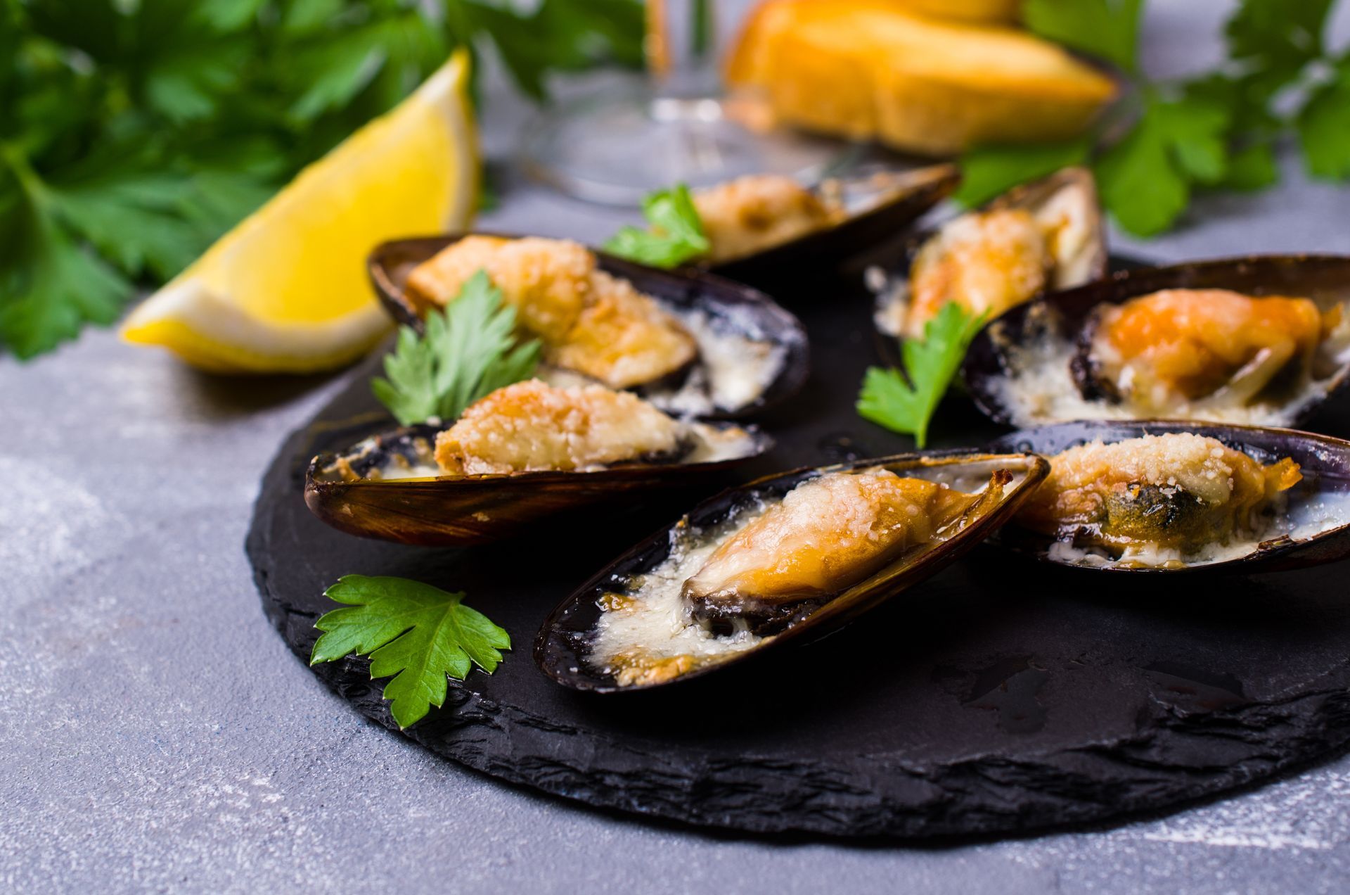 Cozze grigliate su un piatto nero con limone e prezzemolo.
