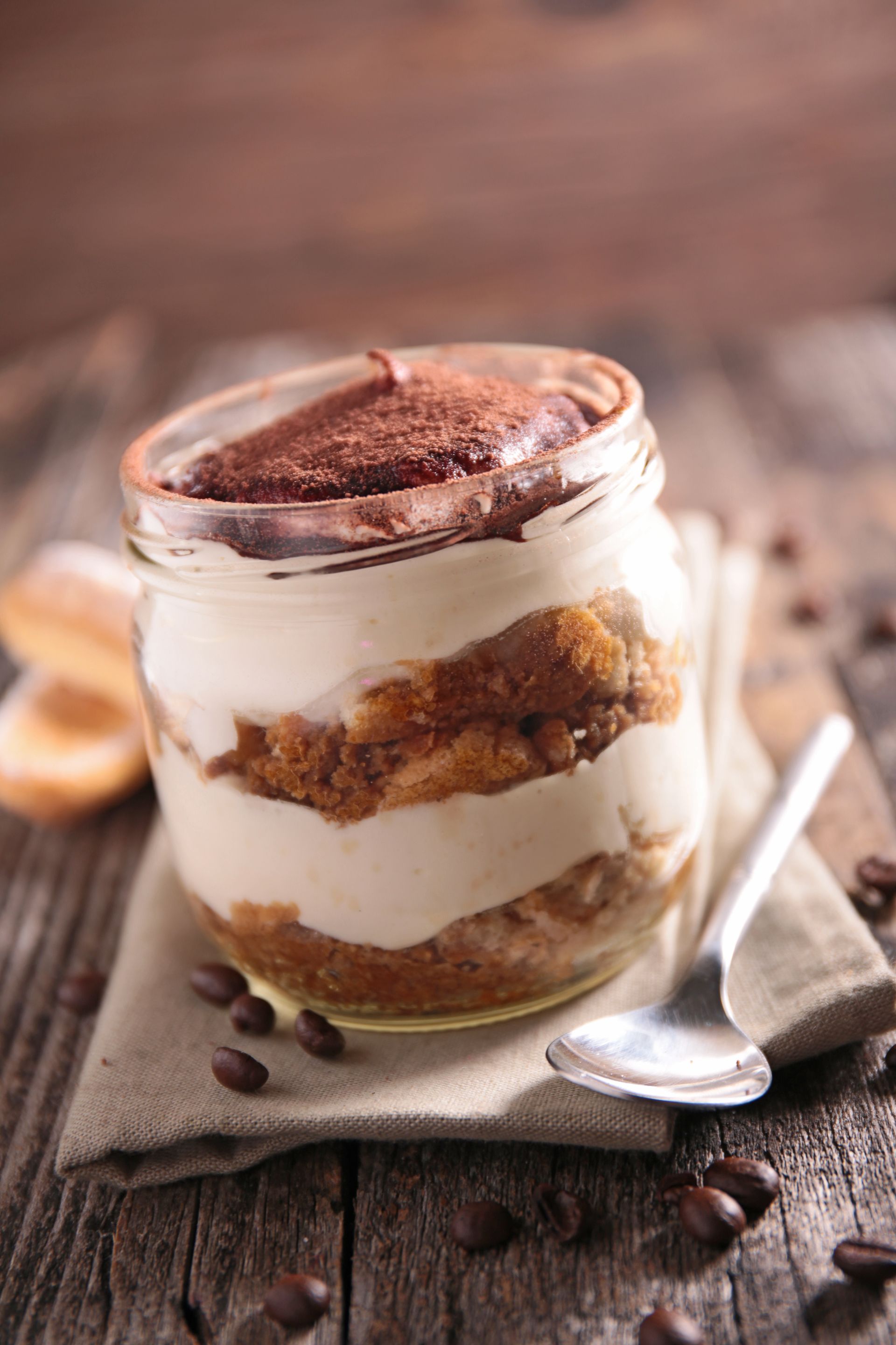 Un barattolo di tiramisù con un cucchiaio e chicchi di caffè su un tavolo di legno.