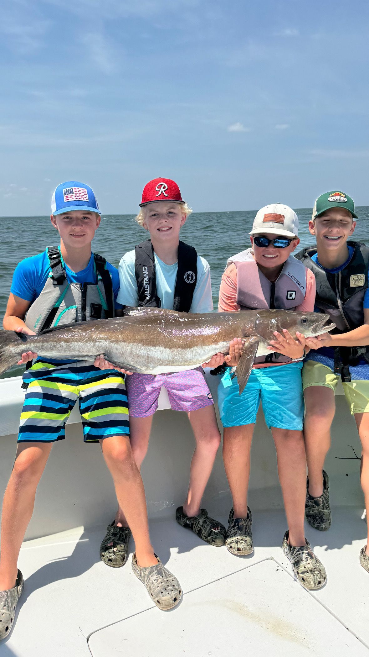 A group of children are sitting on a boat holding a large fish.