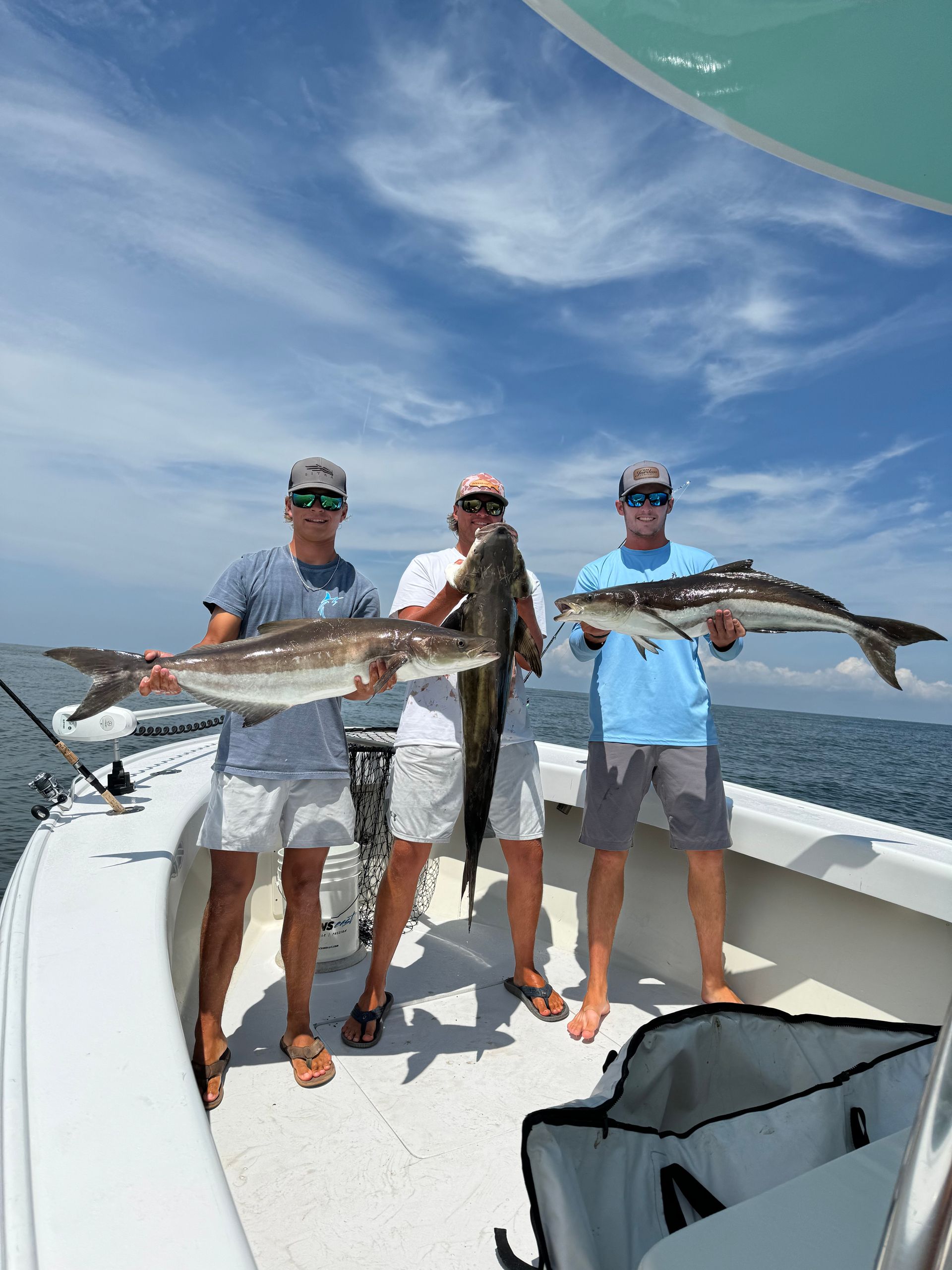 Three men are standing on a boat holding large fish.