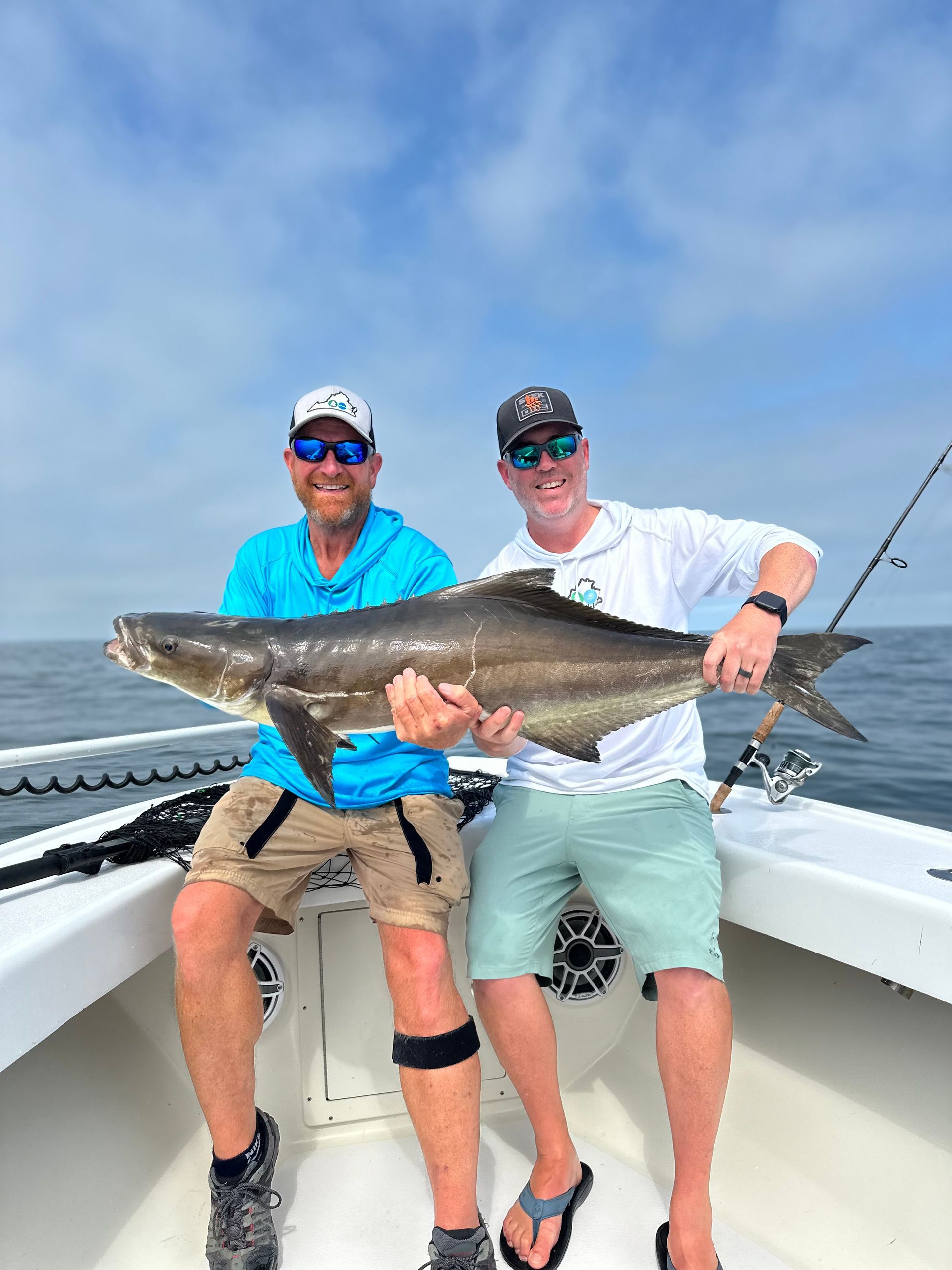 Two men are sitting on a boat holding a large fish.