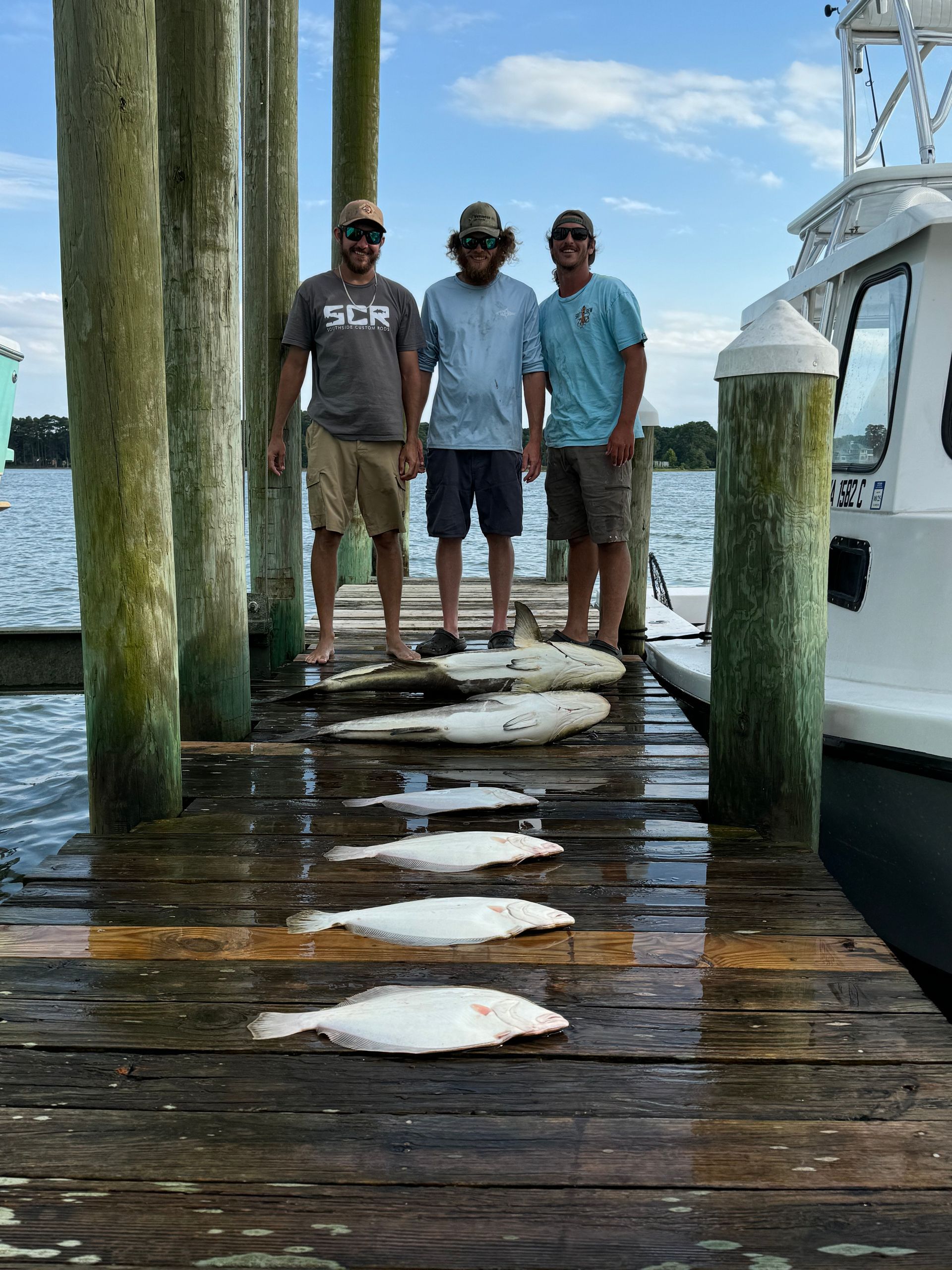 Three men are standing on a dock with fish on it.