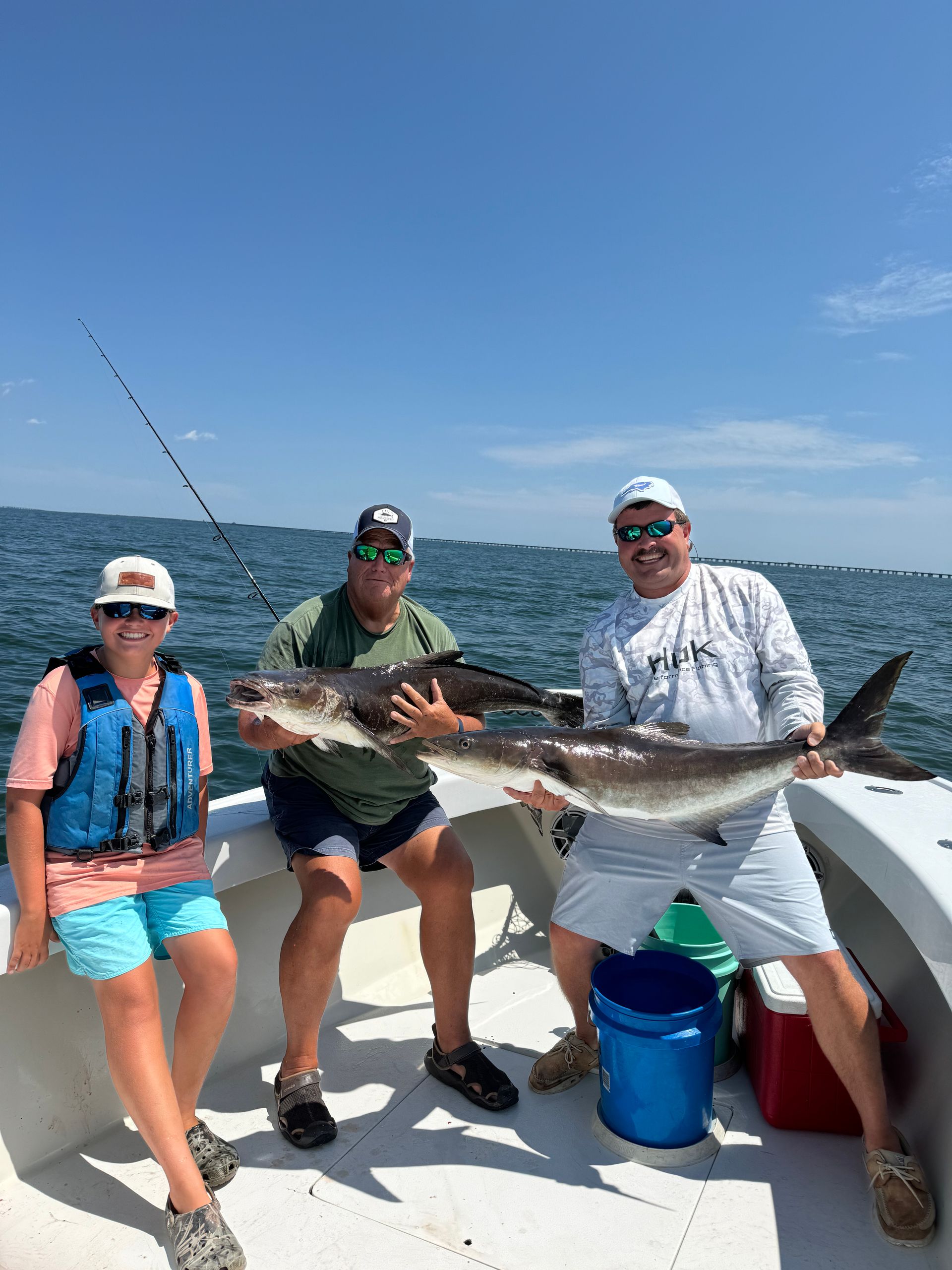 Three people are sitting on a boat holding a large fish.