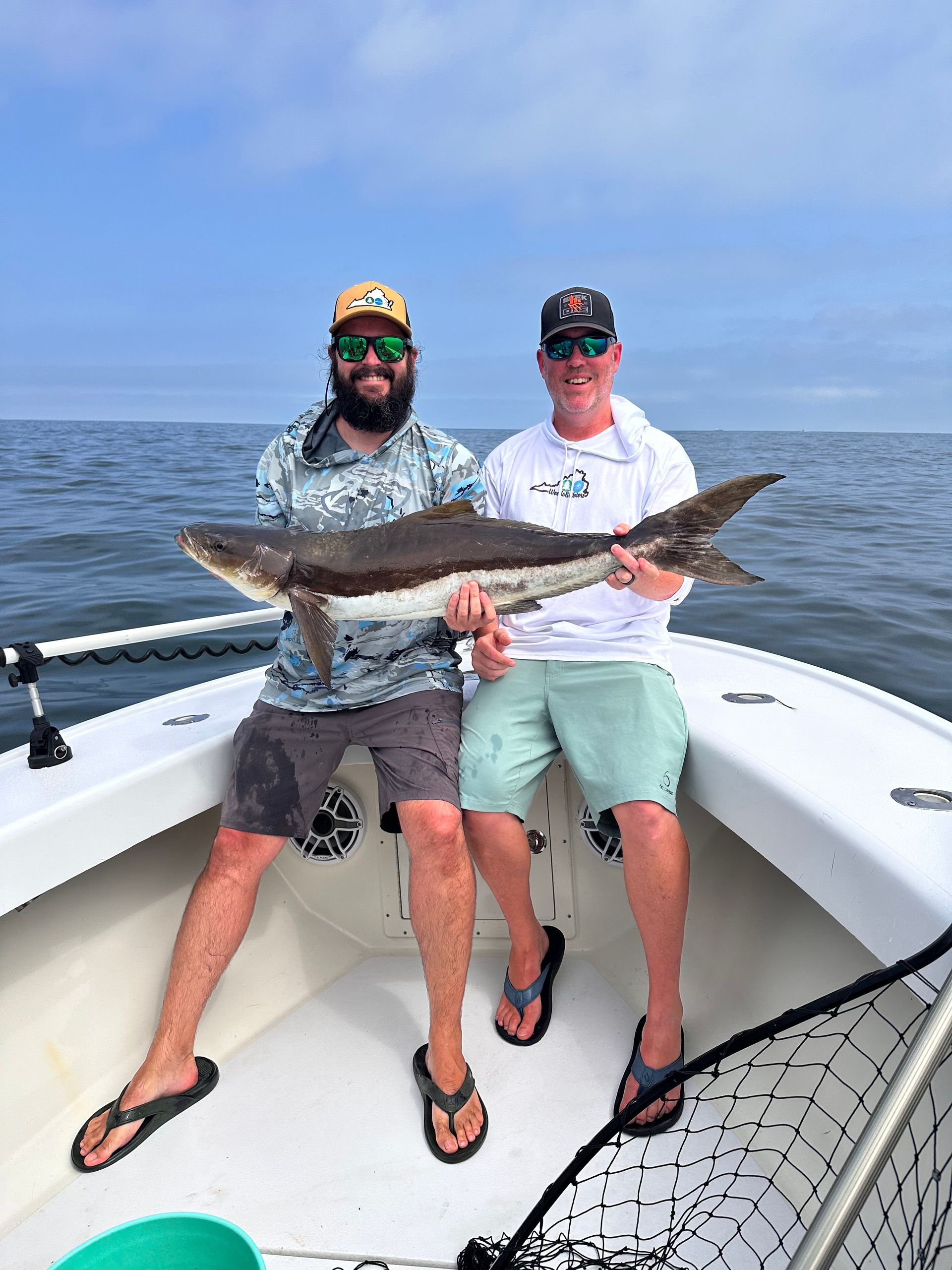 Two men are sitting on a boat holding a large fish.