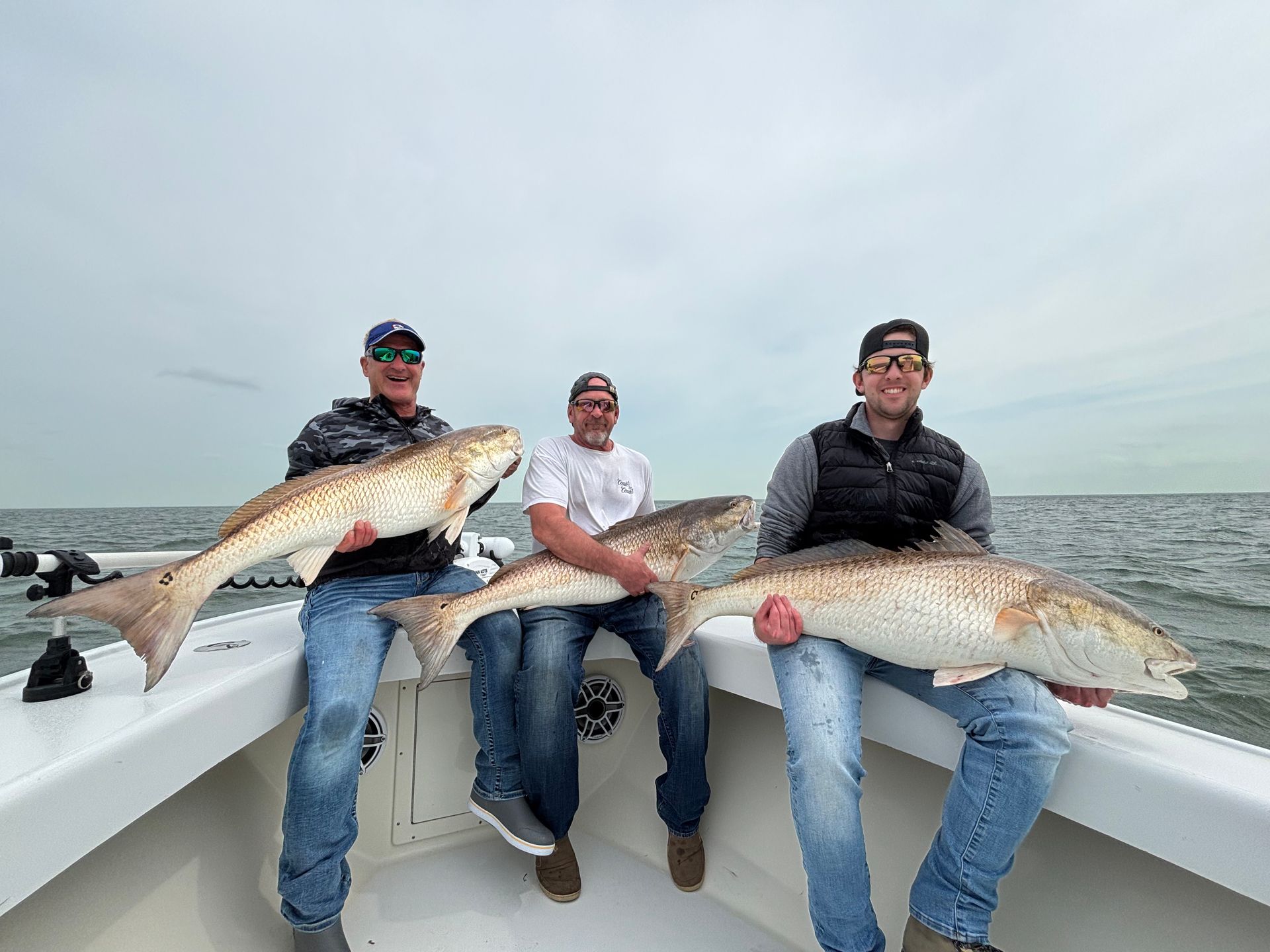 Three men are sitting on a boat holding large fish.