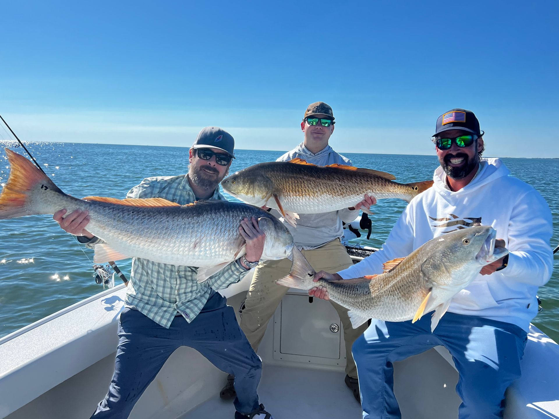 Three men are sitting on a boat holding large fish.
