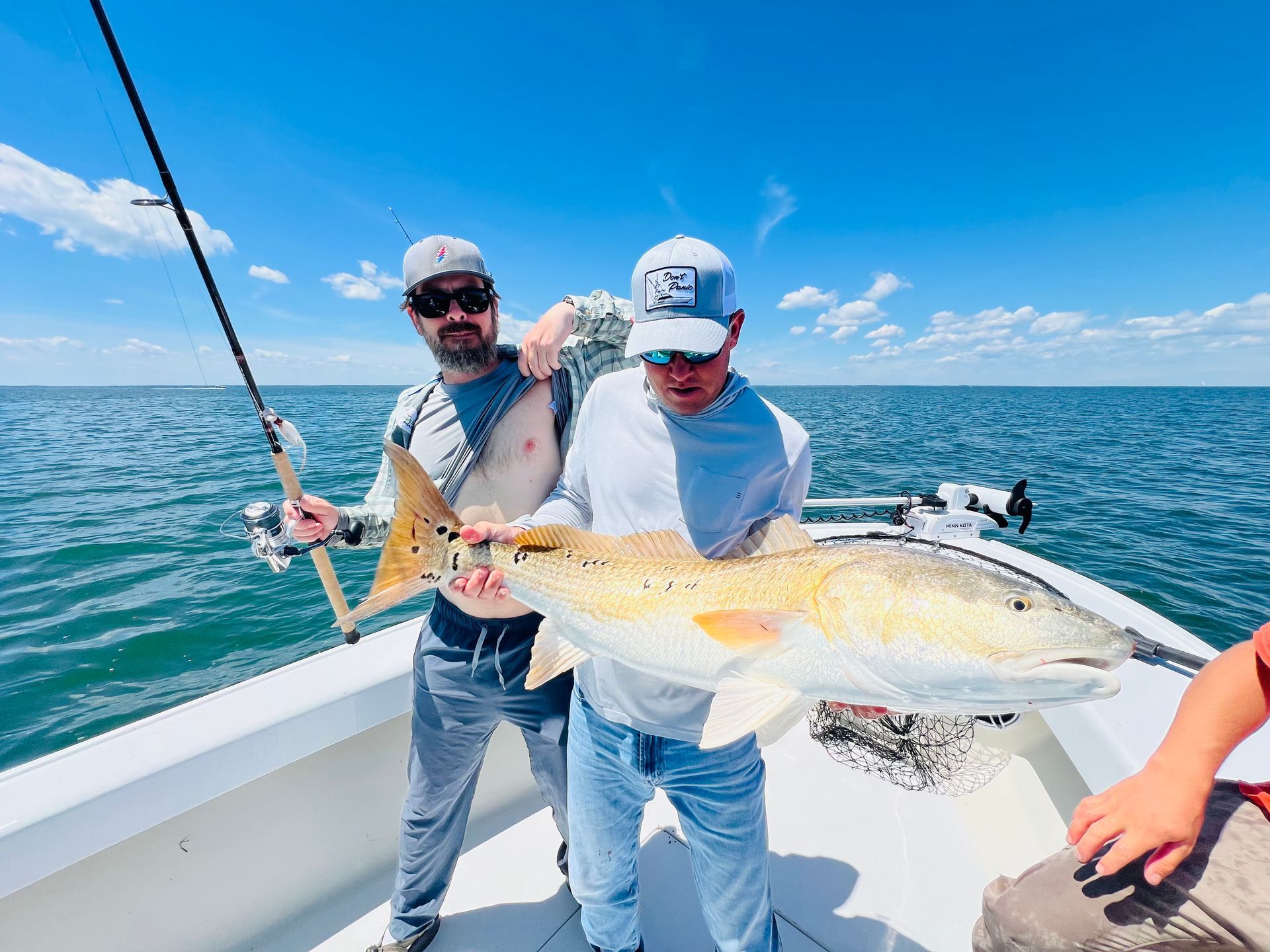 Two men are standing on a boat holding a large fish.