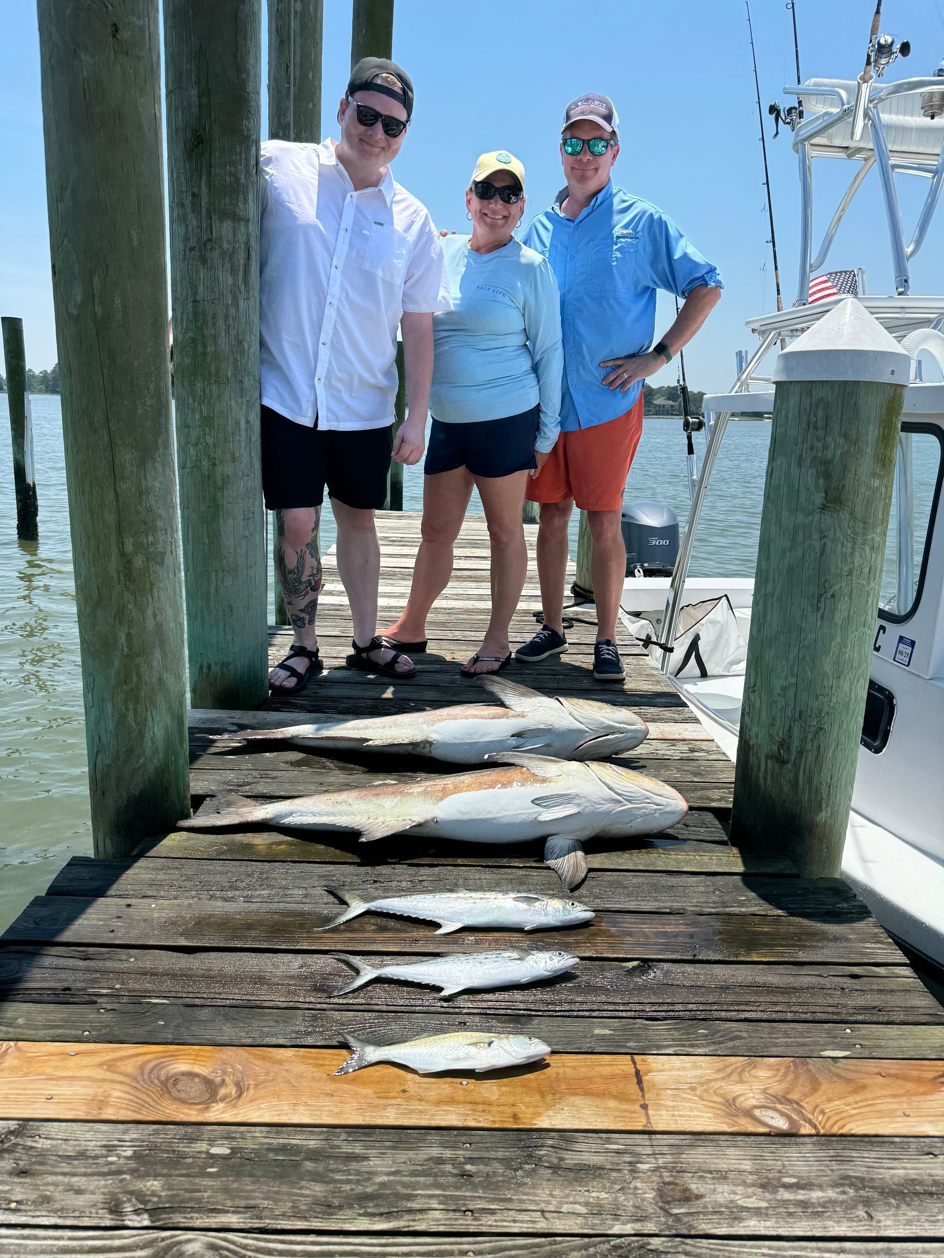 A group of people standing on a dock with fish on it.