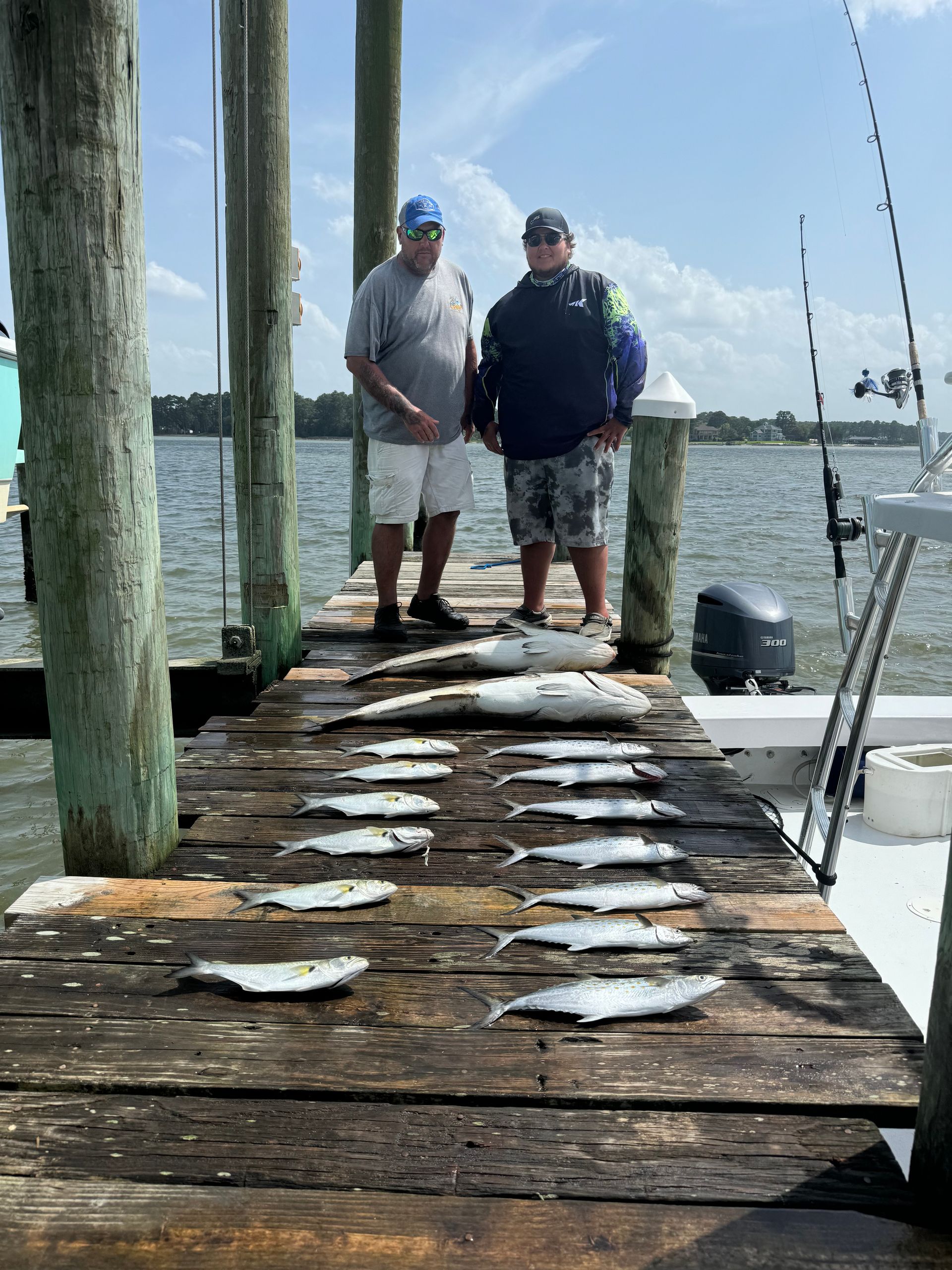 Two men are standing on a dock with fish on it.