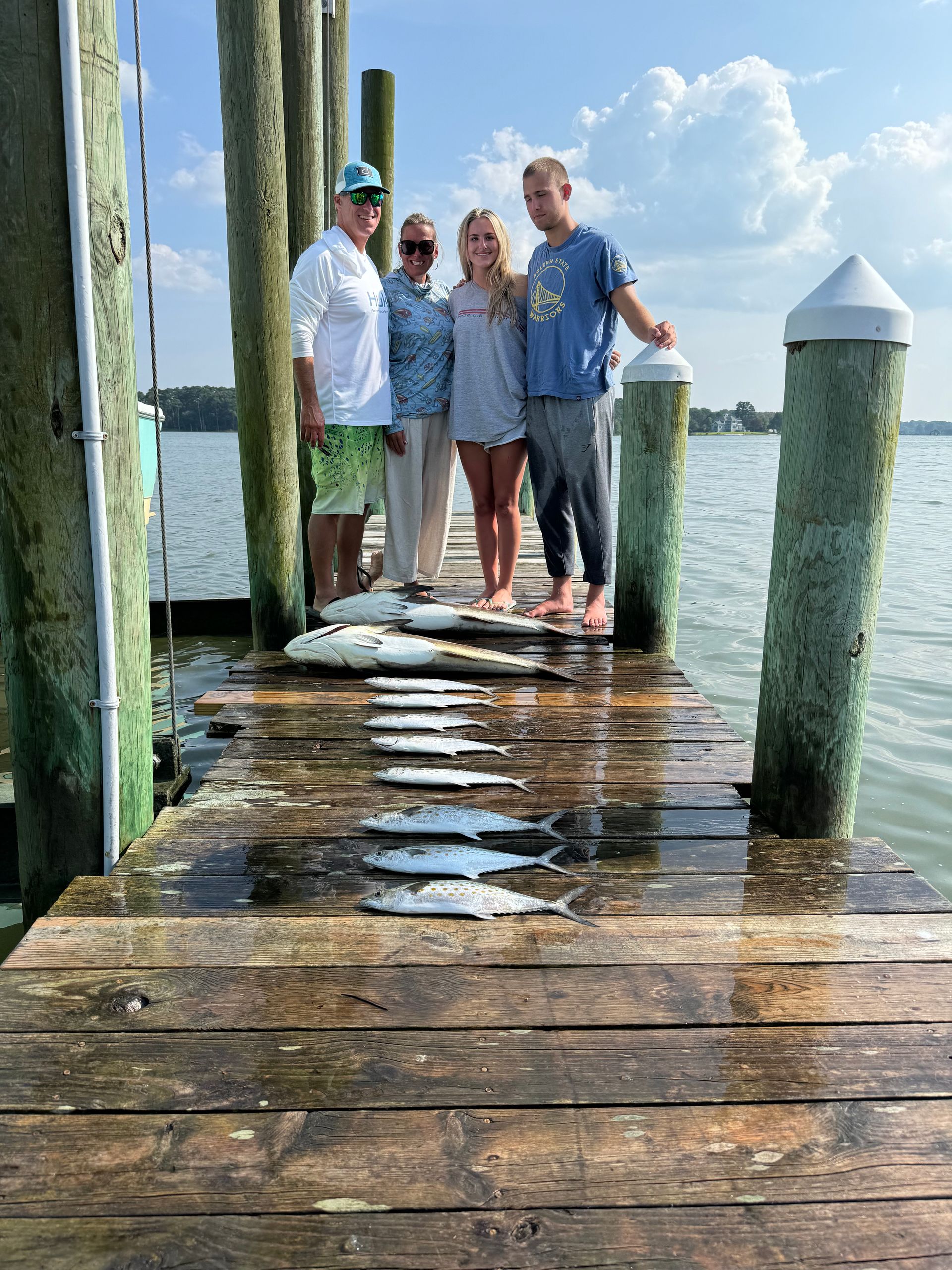 A group of people are standing on a dock holding fish.