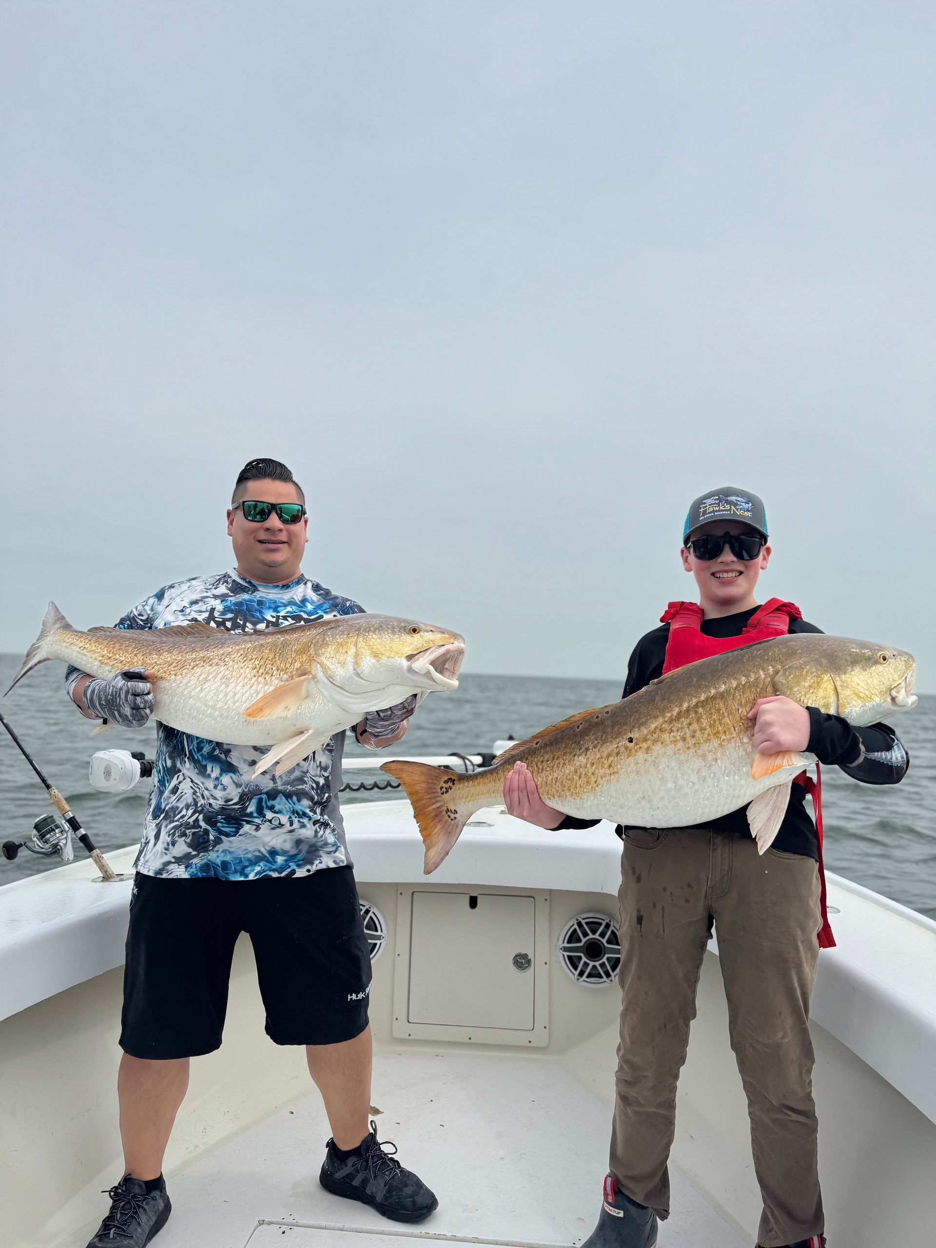 Two men are standing on a boat holding large fish.