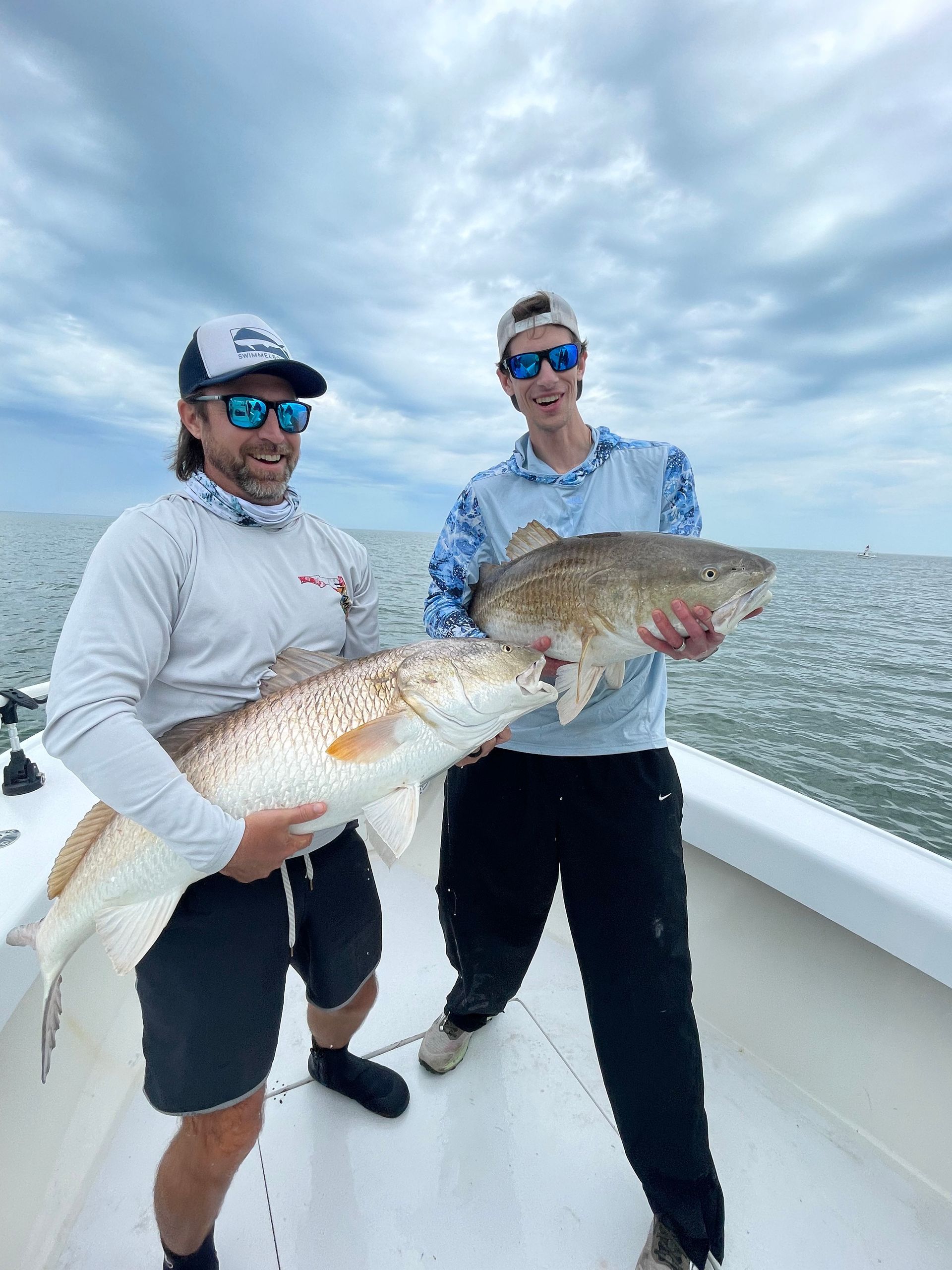 Two men are standing on a boat holding a large fish.