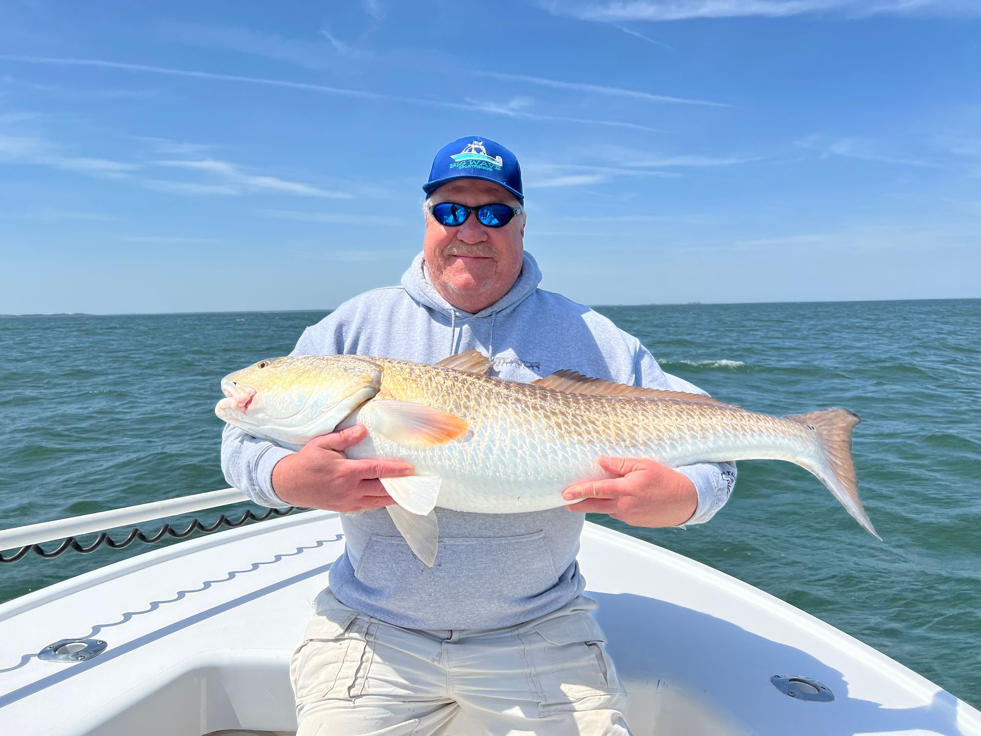 A man is holding a large fish on a boat in the ocean.