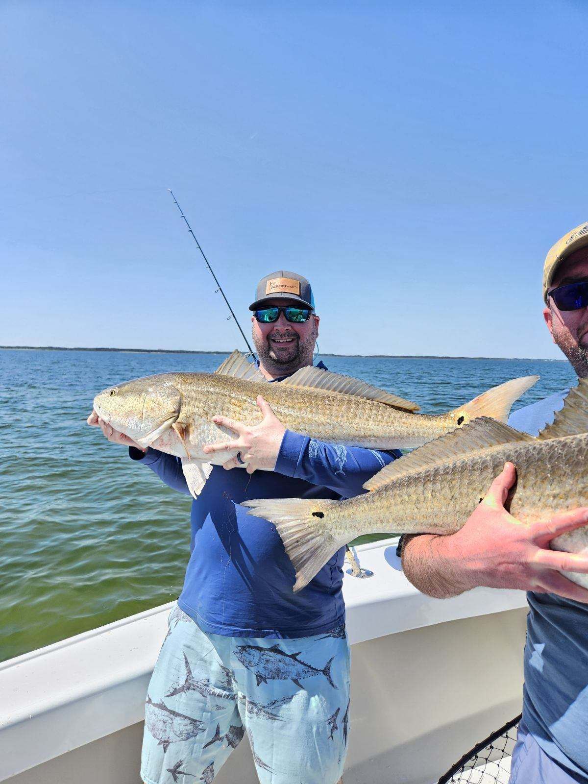 Two men are holding redfish on a boat in the water.