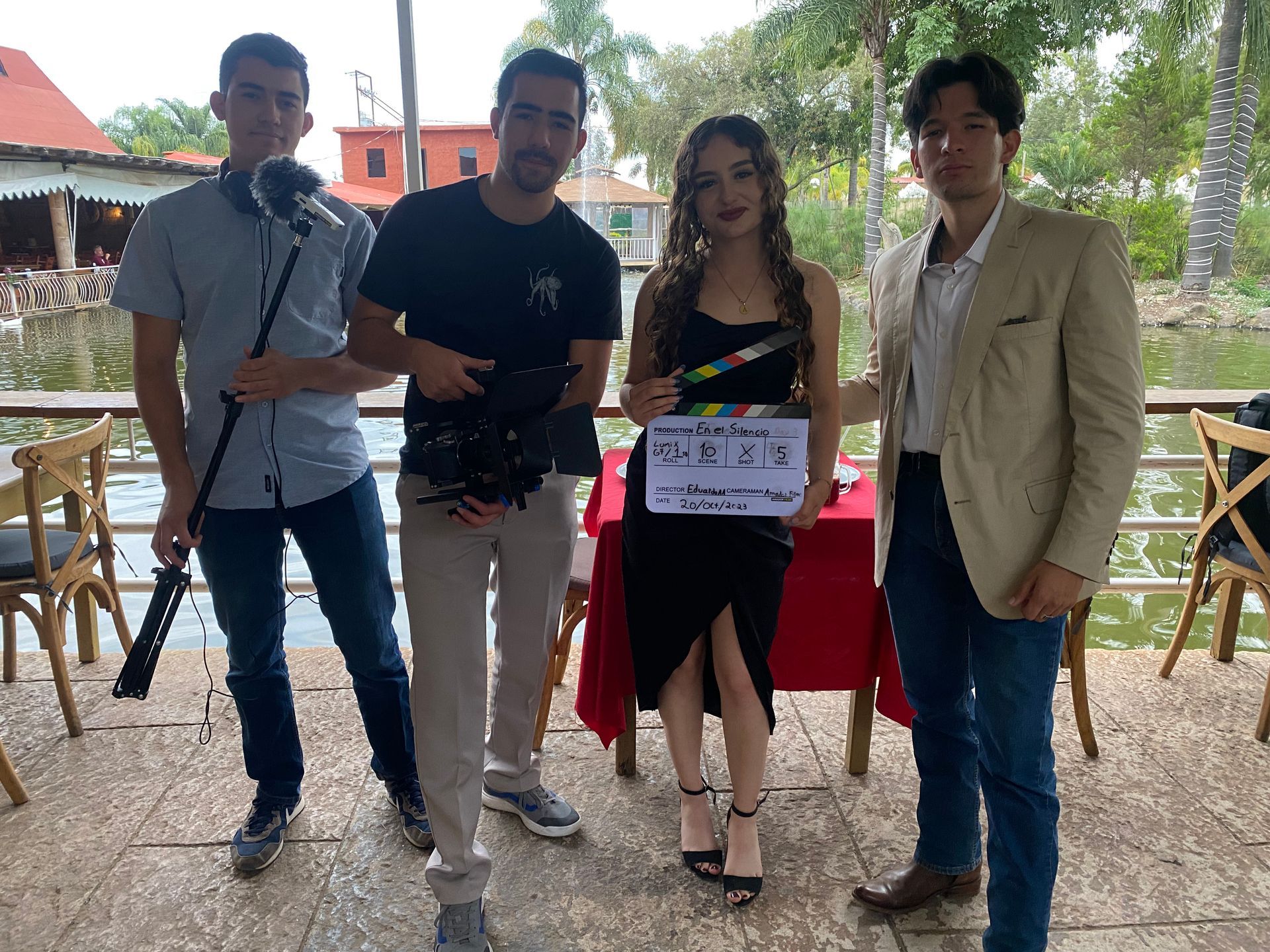 Un grupo de personas de pie alrededor de una mesa con una mujer sosteniendo una claqueta.