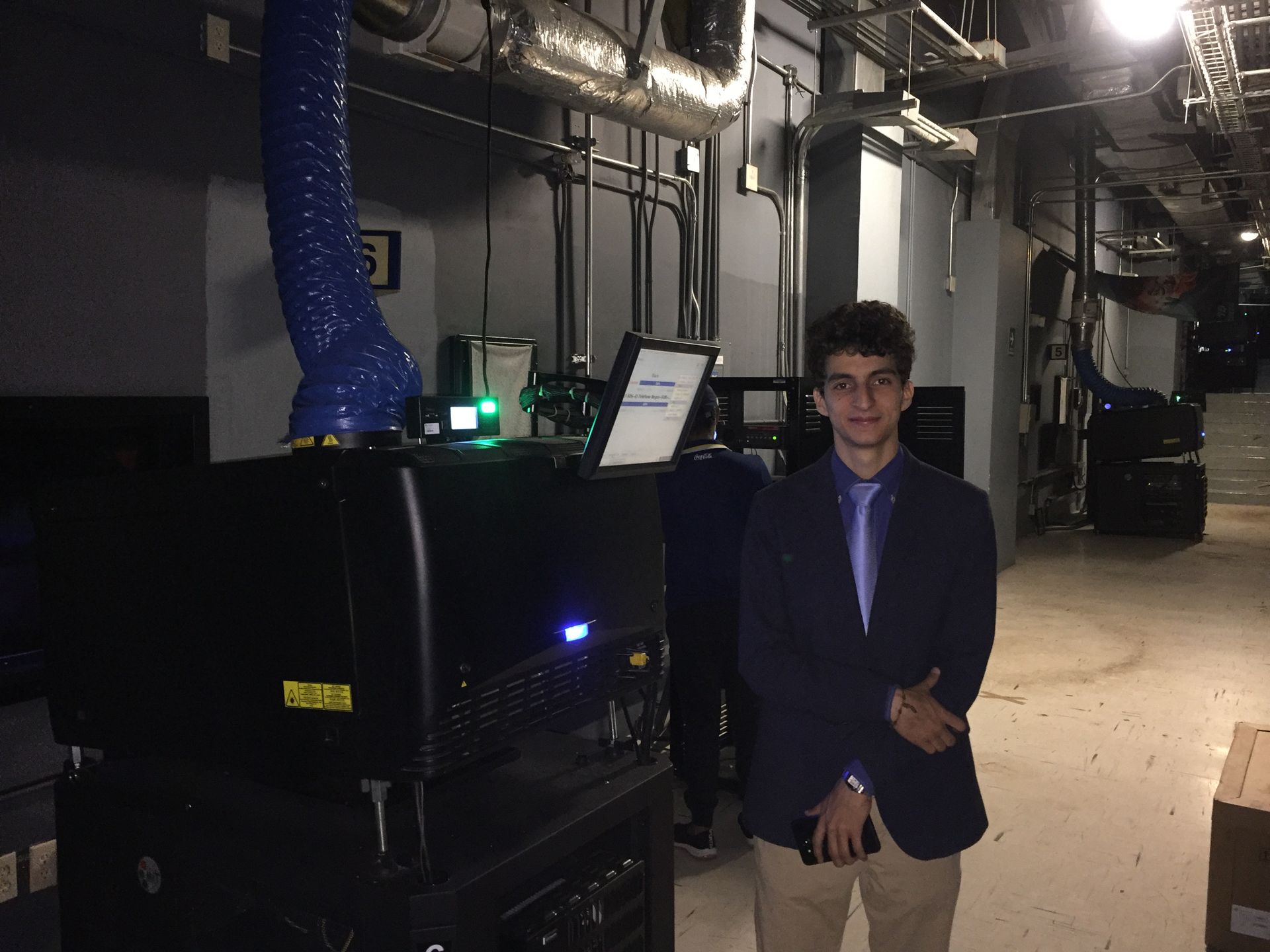 Un joven con traje y corbata está de pie en una habitación oscura.
