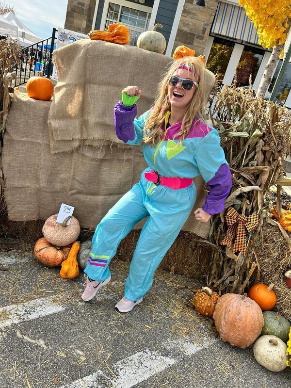 A woman in a blue jumpsuit is standing in front of pumpkins.