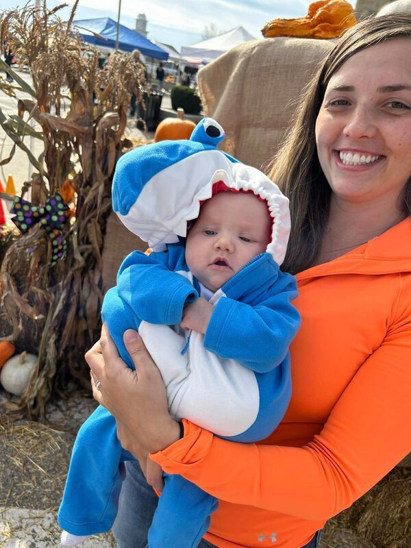 A woman is holding a baby in a shark costume.
