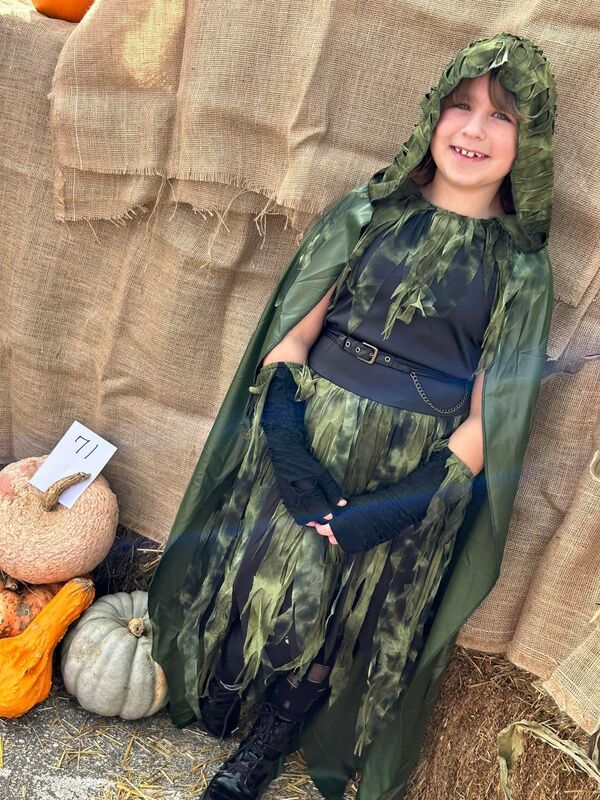 A little girl in a camouflage costume is sitting on a pile of hay.