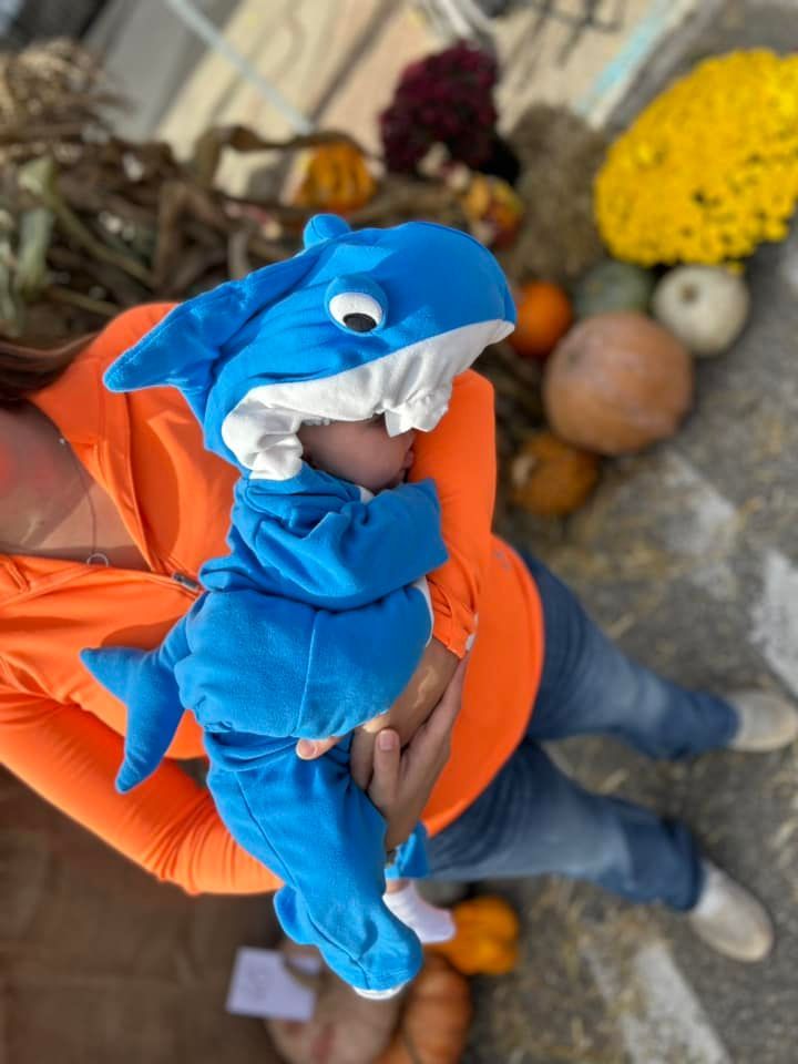A woman is holding a baby dressed in a shark costume.