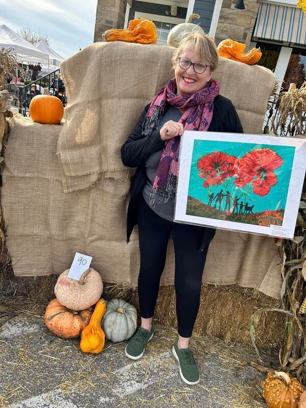 A woman is holding a painting of a group of people standing next to pumpkins.