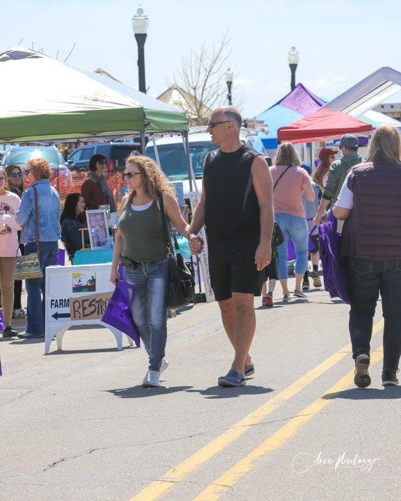 People walking down a street in front of a sign that says farmers market