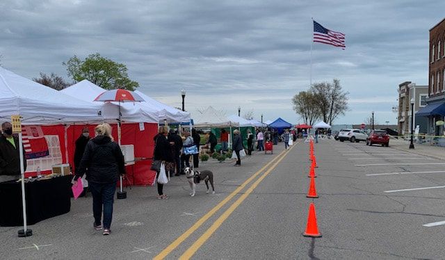 A group of people are walking down a street lined with tents and cones.