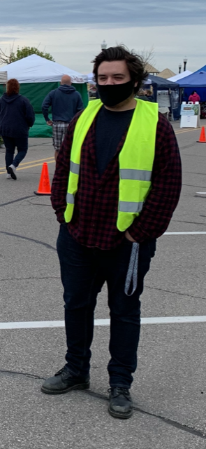 A man wearing a mask and a yellow vest stands in a parking lot
