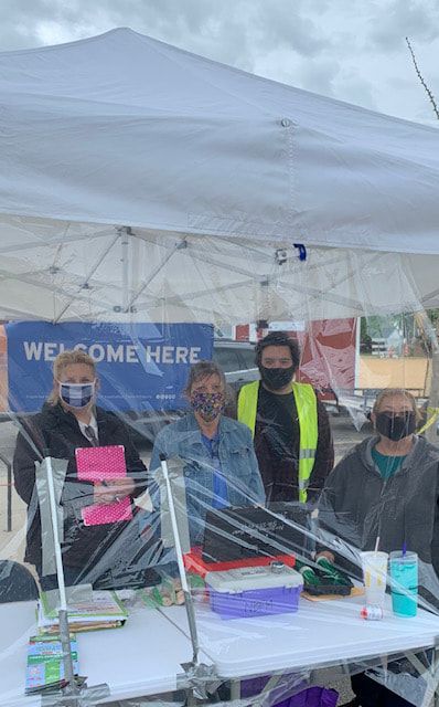 A group of people wearing masks are standing around a table under a tent.