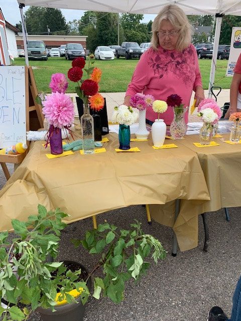 A woman in a pink shirt is standing behind a table with vases of flowers on it