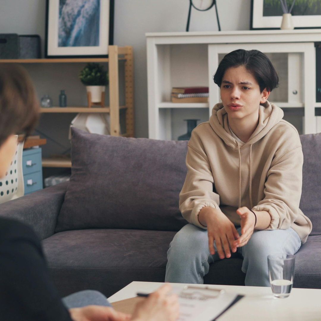 A woman is sitting on a couch talking to another woman