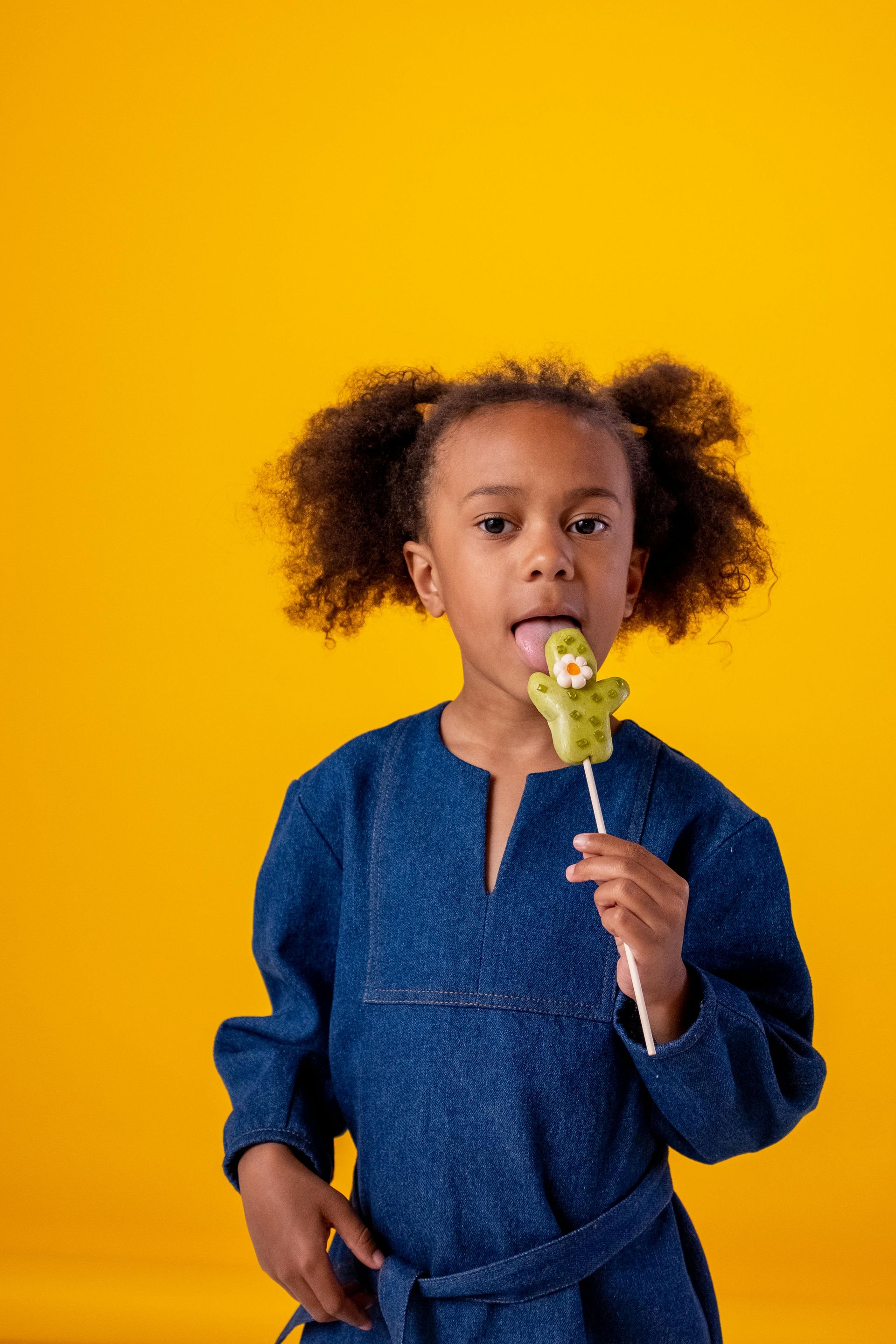 A little girl is holding a lollipop in her mouth.