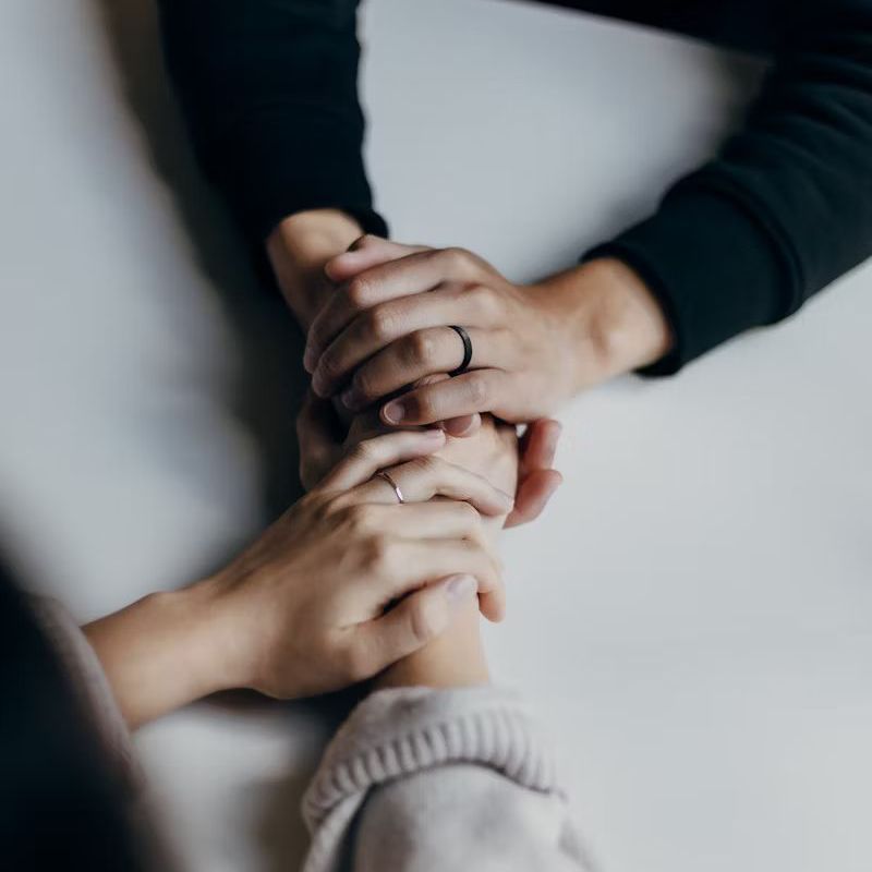 Two people holding hands, offering comfort and support. One person wears a black sweater, the other a light sweater.
