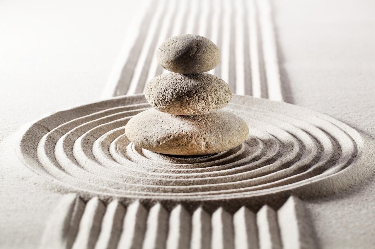 Three rocks are stacked on top of each other on a sandy surface.