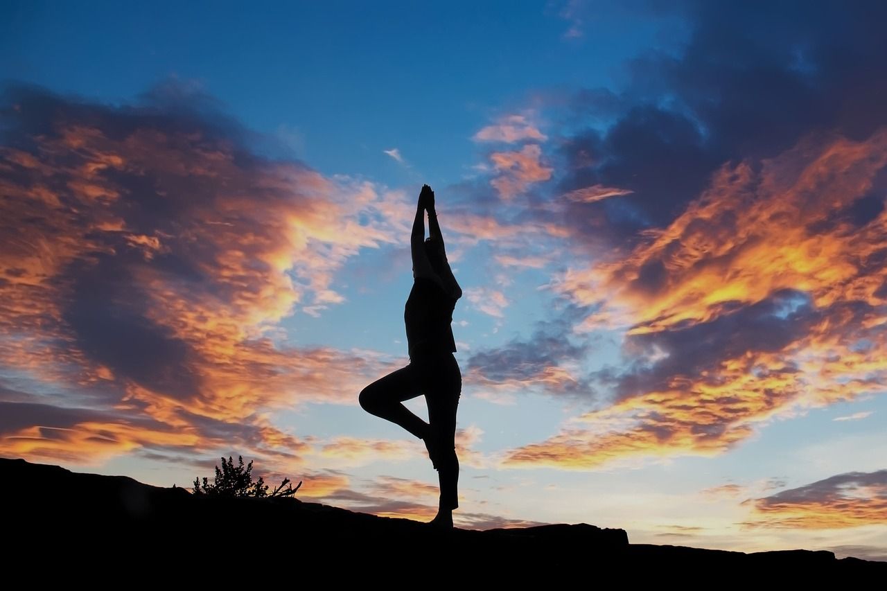 A silhouette of a woman doing a yoga pose at sunset.