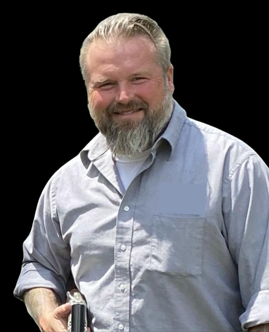 A man with a beard is wearing a blue shirt and holding a book.