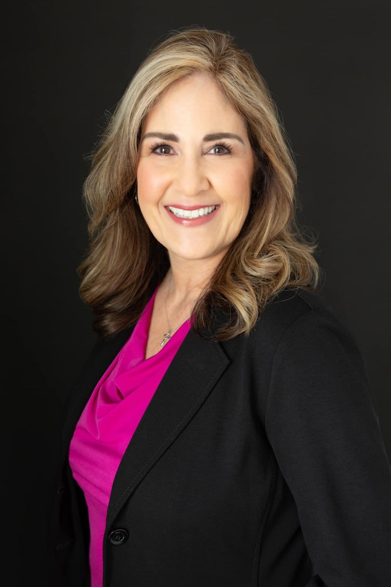 A woman wearing a black jacket and a pink shirt is smiling for the camera.