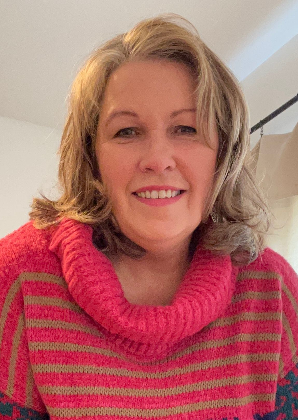 A woman is wearing a pink sweater and smiling for the camera.