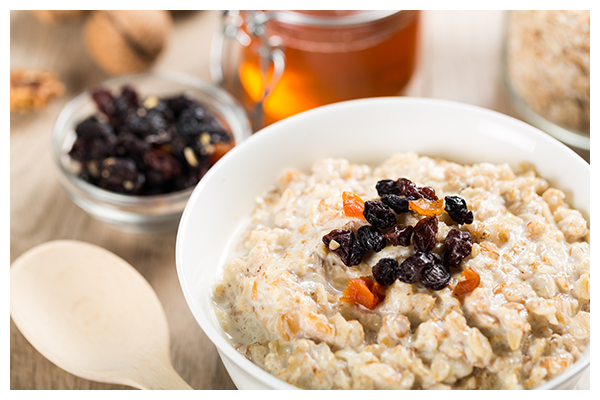 a bowl of oatmeal with raisins and nuts next to a jar of honey .