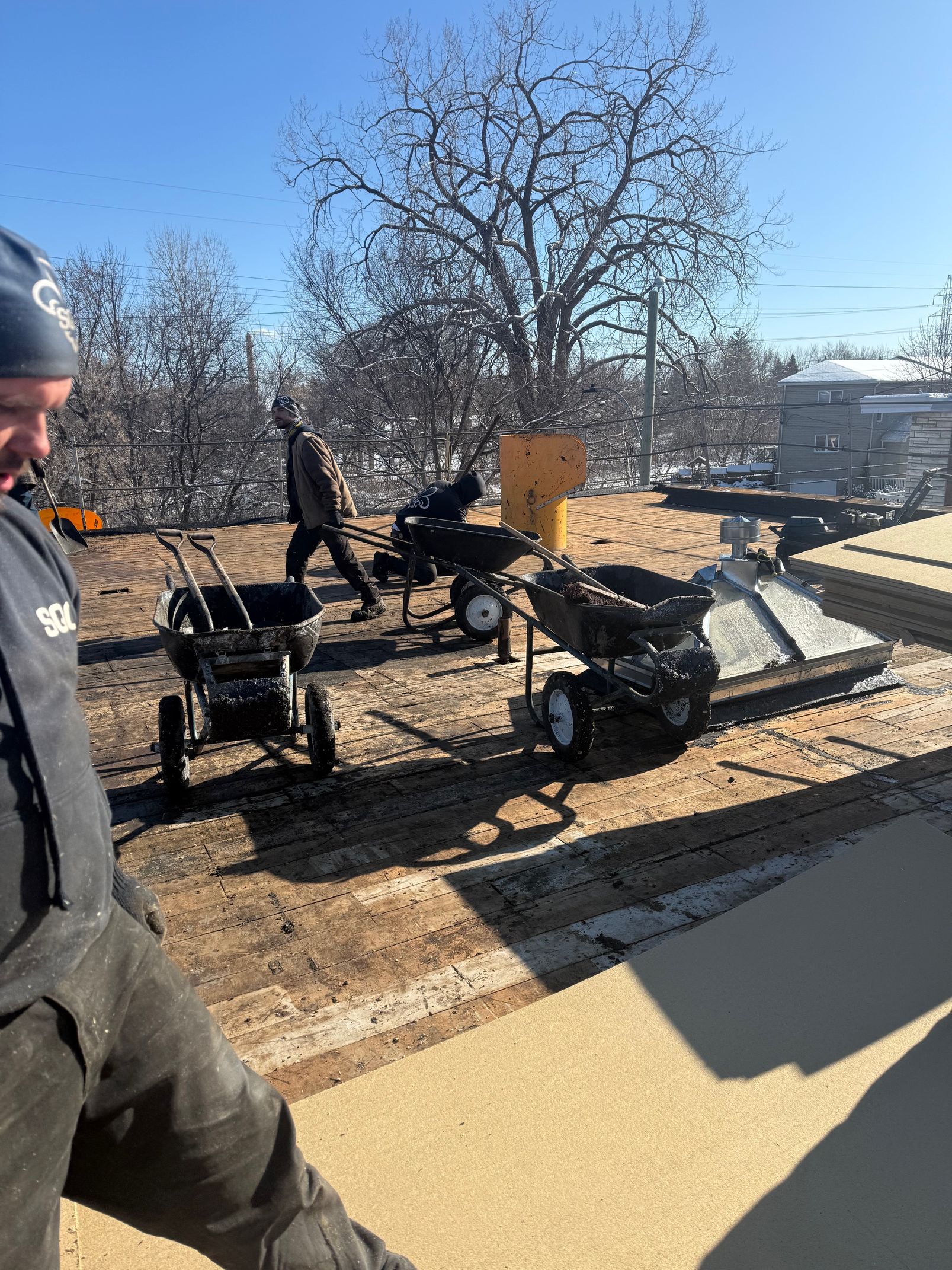 Un homme se tient debout sur un toit à côté d'une souffleuse à neige.